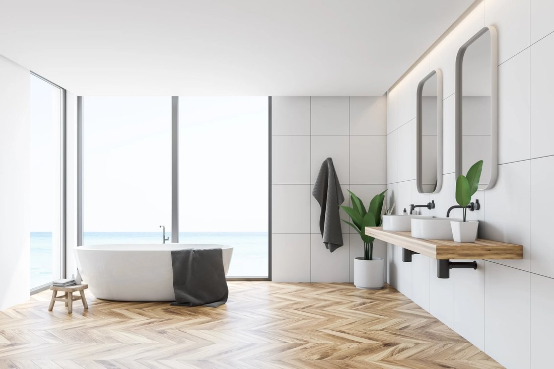 Bagno con vasca bianca freestanding, parquet a spina di pesce, doppio lavabo su mensola in legno e vetrate sul mare