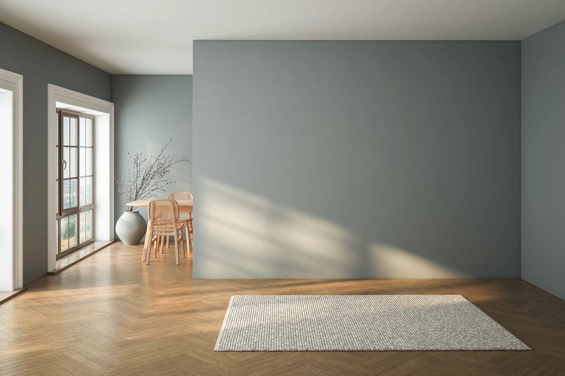 Ambiente vuoto con pareti grigio-azzurre, parquet a spina di pesce, tappeto chiaro e tavolo con sedie in legno e paglia